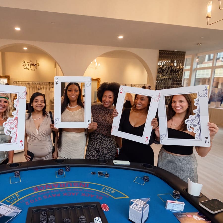 Bachelorette party guests posing with oversized playing-card photo frames behind the table